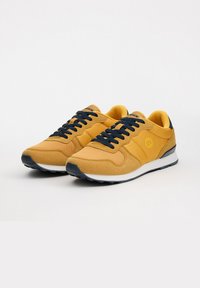 Zapatillas deportivas amarillas con una combinación de materiales de ante y malla, punta redonda, cordones azul marino y una suela intermedia blanca.