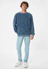 Sudadera azul de tejido suave con un corte relajado, cuello redondo y mangas largas. Combinada con pantalones vaqueros azul claro y zapatillas blancas.