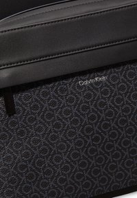 Borsa in pelle nera con motivo 'CK' in rilievo, caratterizzata da un pannello superiore liscio, design elegante e dettaglio del logo Calvin Klein in argento.