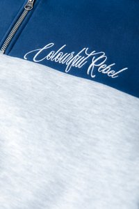 Blauwe en lichtgrijze sweatshirt met een rits, voorzien van witte geborduurde tekst "Colourful Rebel" over de borst. Zachte katoenen stof.