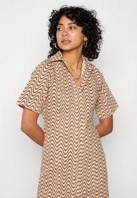 Vestido padrão de ondas castanho e bege, com mangas curtas, design com colarinho, frente com botões, textura suave, até ao joelho.