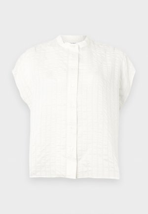 Valkoinen lyhythihainen pusero, jossa on kuvioitu ruutukuvio, mandariinikaulus ja etuosan napitus.