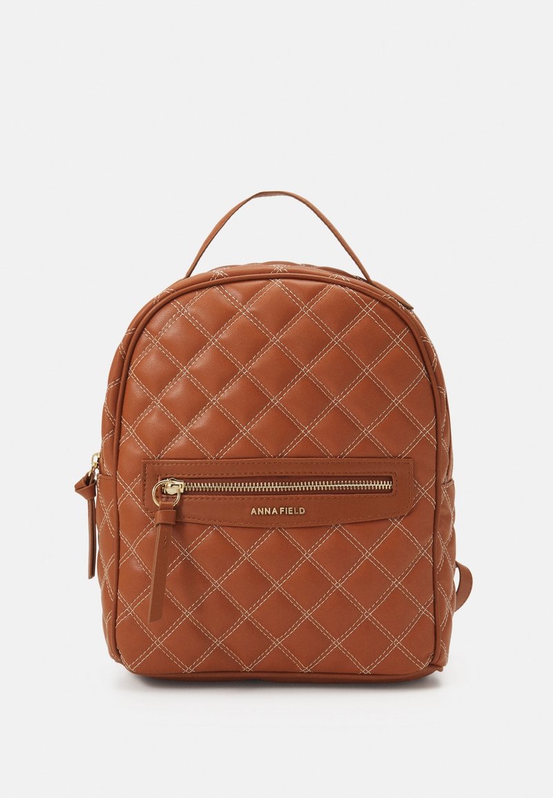 Sac à dos marron en similicuir matelassé avec une poche zippée à l'avant, des accessoires dorés et une poignée supérieure. Présente un motif de couture diagonale.