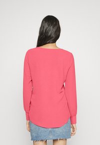 Top de manga longa, cor-de-rosa, com decote arredondado e bainha curva, combinado com uma saia de ganga. Textura de tecido suave, design simples.