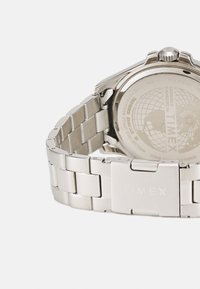 Reloj de acero inoxidable con brazalete de metal; esfera redonda, diseño de globo grabado en la parte posterior, resistente al agua hasta 100 metros.