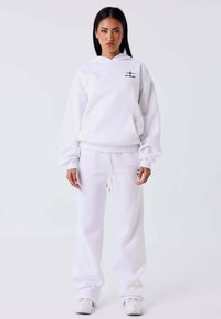 Witte sweatshirt en bijpassende joggingsbroek van zachte stof. De sweatshirt heeft een voorzak en een capuchon; de joggingsbroek heeft een taille met trekkoord.