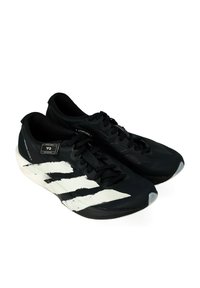 Un paio di scarpe da corsa atletiche nere con design a strisce bianche, lacci neri e dettagli del marchio sui lati e sulla linguetta.