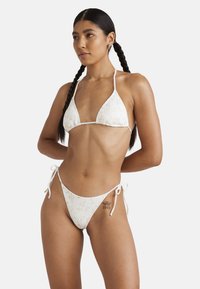 Biely rebrovaný bikiny set s trojuholn�íkovým vrchom a nastaviteľnými bokmi na viazanie, zdobený jemným kvetinovým vzorom.