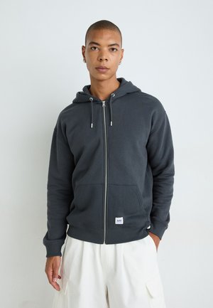 Gray zip-up hoodie made of soft fabric featuring a front pocket, drawstring hood, and ribbed cuffs. Subtle brand label at the hem.