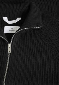 Melnā rāvējslēdzēja džemperis ar ribota tekstūra. Ar augstu apkakli, sudraba rāvējslēdzēja detaļu, un zīmolu "Matinique" uz etiķetes.