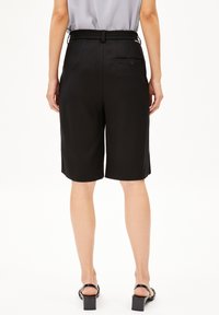 Schwarze Bermudashorts mit elastischem Bund, glatter Textur und einer kleinen Tasche auf der Rückseite mit einem Knopfdetail.