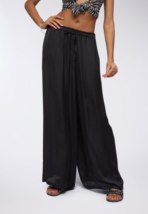 Pantaloni neri a gamba larga con una texture liscia e fluida e una vita elastica. Abbinati a sandali neri con dettagli metallici.