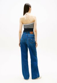 Vaqueros anchos de mezclilla azul con cintura alta, que cuentan con dos bolsillos traseros y una etiqueta de cuero. Combinados con un top corto de tirantes con rayas.