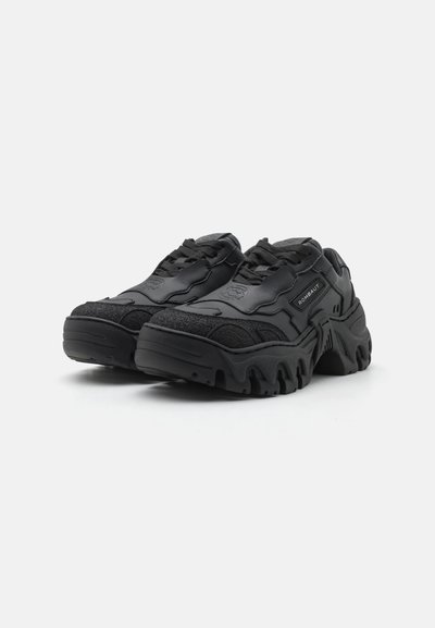 Schwarze Sneaker mit einer Mischung aus strukturierten und glatten Materialien, dicken Sohlen mit ausgeprägten Rillen und einem auffälligen Schnürsystem.