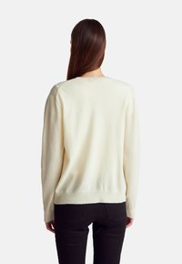 Śmietankowy sweter dzianinowy z okrągłym dekoltem i długimi rękawami, o luźnym kroju i prążkowanych mankietach. Nosić go na ciemnych dżinsach.