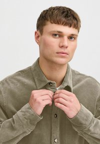 Kordfløjlsskjorte i en dæmpet olivengrøn farve, med button-down krave, frontknapper og lange ærmer med knapmanchetter. Tekstureret stof synligt.