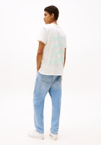 Hvid bomulds t-shirt med oversize mintgrøn tekst på ryggen. Parret med lyseblå denim jeans og hvide sneakers.