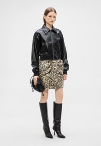 Melna ādas bombers jaka ar rāvējslēdzēju, leoparda raksta wrap svārki, melni ceļgalu augsti zābaki ar papēžiem, turot nelielu melnu rokassomu.