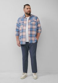 Blauwe en roze geruite button-up shirt met opgerolde mouwen, gedragen over een witte T-shirt, gecombineerd met marineblauwe broek en beige sneakers.