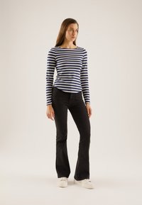 Striped long-sleeve top in navy and white, paired with black flared jeans. The outfit features a simple design and a comfortable fit.