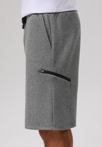 Šedé bavlněné šortky s elastickým pasem, bočními kapsami a kapsou na zip na pravé nohavici. Hladká textura, design do délky kolen.