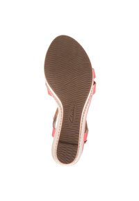 Suola in gomma marrone con grip testurizzato, presenta cinturini alla caviglia rosa e un bordo inferiore beige chiaro. Logo Clarks visibile sulla suola.