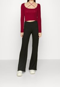 Burgundowa, prążkowana, długa bluzka crop z okrągłym dekoltem i skrzyżowanymi ramiączkami, zestawiona z czarnymi, teksturowanymi spodniami typu wide-leg oraz białymi sneakersami.