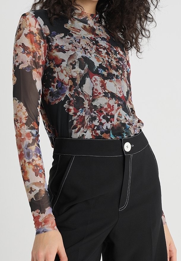 Haalimaton pitkähihainen paita, jossa on monivärinen kukkakuosi mustalla taustalla, yhdistettynä korkeavyötäröisiin mustiin housuihin, joissa on valkoiset saumat.