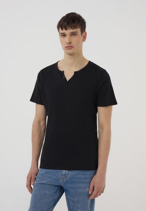 T-shirt nera a maniche corte con scollo a V e due bottoni, realizzata in tessuto morbido, abbinata a jeans di denim blu chiaro.