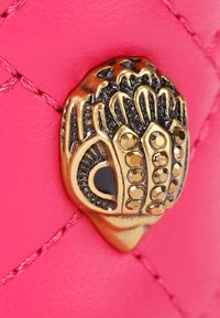 Różowa skórzana dekoracja z pikowanym wzorem, z akcentem w postaci mosiężnego uchwytu w kształcie dłoni ozdobionego kamieniami szlachetnymi i czarnymi detalami.