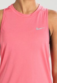 Canotta atletica senza maniche rosa con scollatura rotonda, realizzata in tessuto morbido, con un logo riflettente argento posizionato sul lato sinistro.