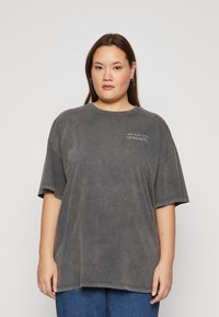 Camiseta de gran tamaño y manga corta en un tejido negro lavado. Presenta un escote redondo y un gráfico textual sutil en el lado izquierdo del pecho.