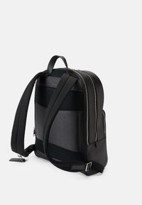 Mochila preta com um acabamento texturizado, apresentando alças de ombro almofadadas, um painel traseiro em malha, zíperes duplos e um design minimalista.