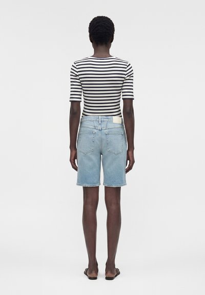 Άτομο που φοράει μαύρη και άσπρη ριγέ κοντομάνικη μπλούζα, ανοιχτό μπλε τζιν σορτς και μαύρα σανδάλια, στέκεται με την πλάτη.