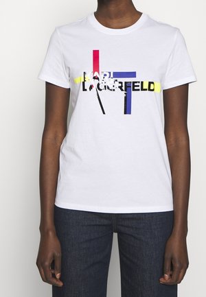 T-shirt en coton blanc avec un imprimé graphique multicolore et le texte noir "KARL LAGERFELD" ainsi que des lignes d'accent géométriques en rouge, bleu et jaune.