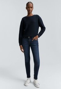 Mornarski pleten pulover z ohlapnim krojem, kombiniran s temno modrimi ozkimi kavbojkami in belimi supergami. Obleka ima preprost, sodoben dizajn.