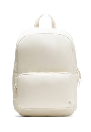 Cream-colored backpack with smooth fabric, rounded shape, two zippered compartments, and a top handle for carrying. Minimalist design.