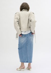 Beige Lederjacke mit Schulterklappen, kombiniert mit einem langen Jeansrock und hellen Sandalen, von hinten betrachtet.