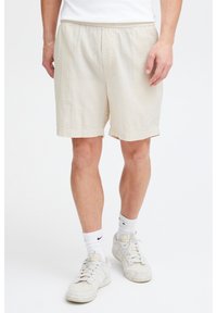 Pantaloni scurți bej texturați cu talie elastică, care ajung până chiar deasupra genunchiului, asortați cu teniși albi și șosete până la gambă.