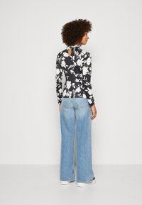 Svart langermet topp med hvit blomsterdesign, detalj med nøkkelhull bak, kombinert med høyhudhøyde lyseblå vide jeans. Jevn tekstur.