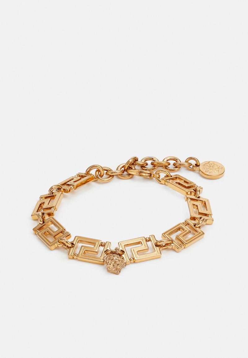 Bracelet en chaîne dorée avec des maillons géométriques, un accent en forme de tête de Méduse et un charm décoratif. Texture lisse avec finition polie.