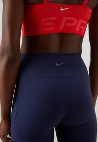 Rød Nike sports-BH med "NIKE PRO"-logo, kombinert med marineblå high-waisted tights som har en subtil grå Nike-logo på midjen.