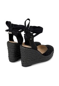 Sandales compensées en suede noir avec une semelle en corde tissée, dotées de liens en tissu sur la cheville et d'un design à bout rond. Accents texturés sur la compensée.