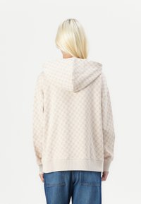 Hellbeige Kapuzenpullover mit einem strukturierten geometrischen Muster, ausgestattet mit einer Kapuze und Bündchenärmeln, kombiniert mit blauen weiten Jeans.