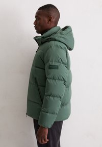 Green puffer jacket with a detachable hood, zippered front, and side pockets. Textured fabric with quilted design. Brand label on sleeve.