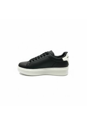 Sneaker in pelle nera con suola spessa bianca e linguetta del tallone bianca con testo nero parziale, vista di profilo su sfondo bianco.