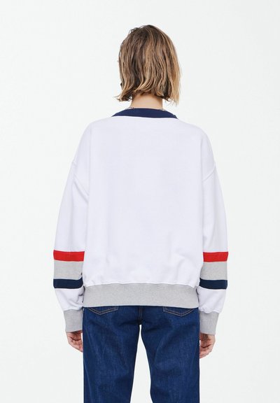 Sweatshirt blanc avec col marine et poignets gris, orné de rayures rouges et bleues. Texture douce, coupe ample et ourlet côtelé.