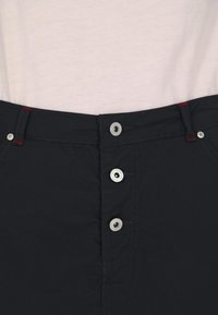 Gonna blu navy a bottoni con dettagli in metallo argentato e cuciture rosse. Tessuto liscio con una forma sagomata e dettagli di cucitura in evidenza.