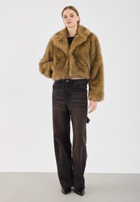 Brun faux fur cropped jakke med bred krave, parret med højtaljede sorte denim jeans og sorte spidse hæle.