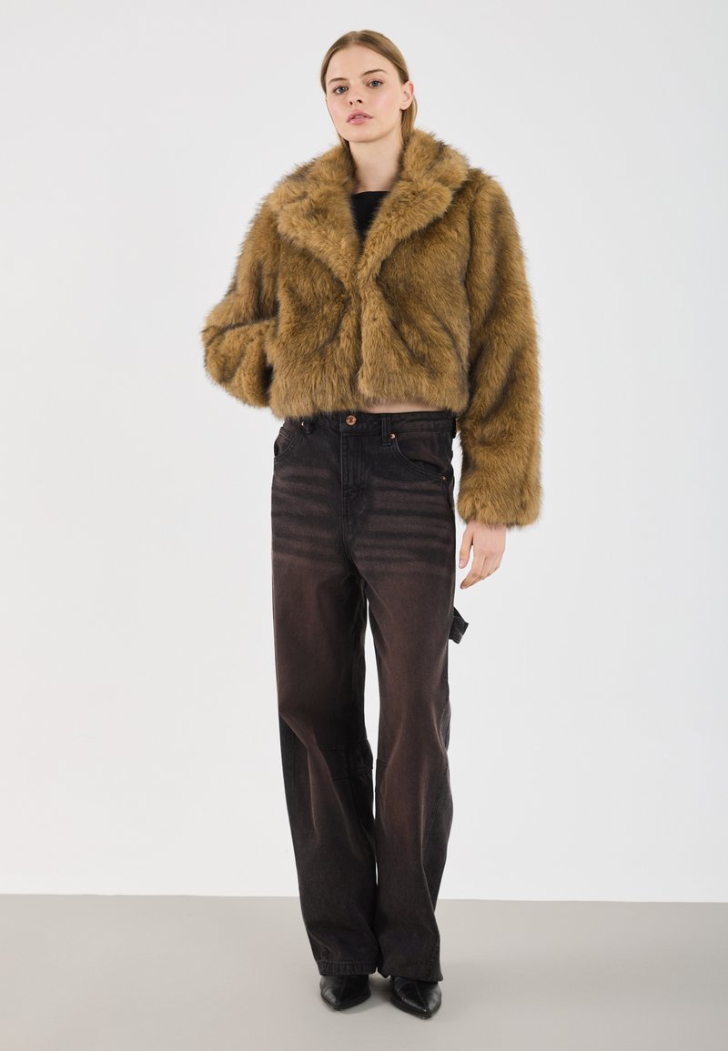 Giacca cropped in finta pelliccia marrone con un ampio colletto, abbinata a jeans in denim neri a vita alta e tacchi neri a punta.